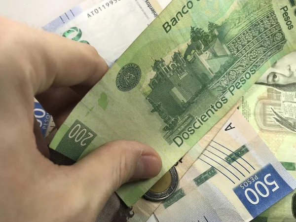 Billetes de pesos mexicanos distribuidos al azar sobre una superficie plana con una mano sobre ellos — Foto de Stock