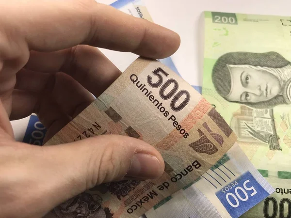 Billetes de pesos mexicanos distribuidos al azar sobre una superficie plana con una mano sobre ellos — Foto de Stock