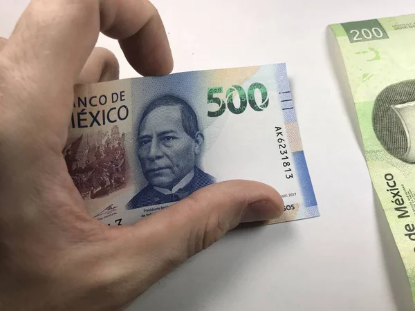 Billetes de pesos mexicanos distribuidos al azar sobre una superficie plana con una mano sobre ellos — Foto de Stock