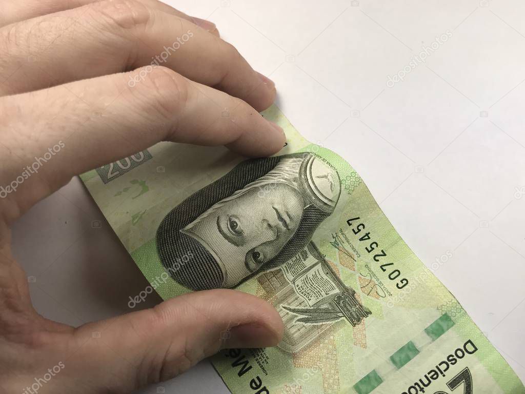 Mexican peso bills spread randomly over a flat surface with a hand over them