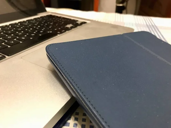 Tablet in een blauwe bekleding over een zilver metallic laptop computer — Stockfoto