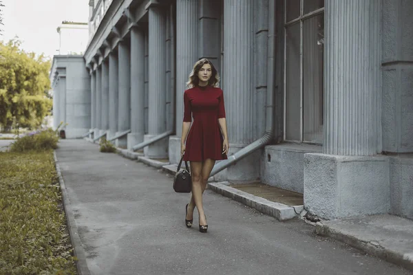 Menina morena elegante bronzeada agradável em vestido curto vermelho com flores está de pé poses e flertando andando na cidade de rua — Fotografia de Stock