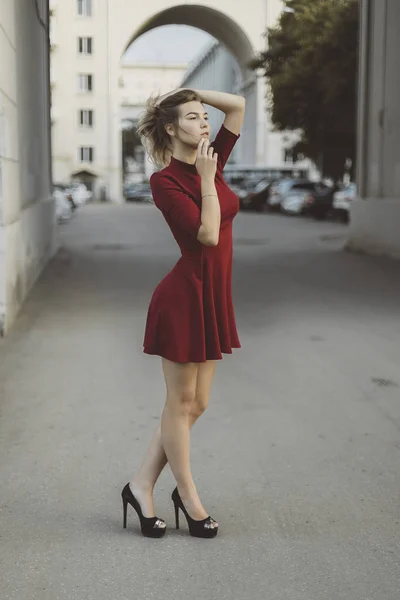 Bella abbronzata ragazza bruna elegante in abito rosso corto con fiori è in piedi pose e flirtare a piedi sulla città di strada — Foto Stock