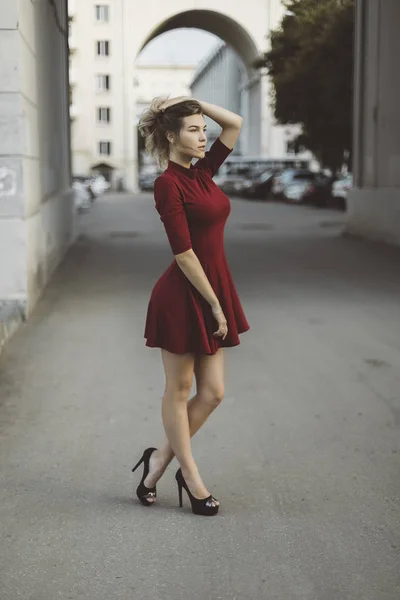 Nice tanned stylish brunette girl in red short dress with flowers is standing poses and flirting walking on the street city