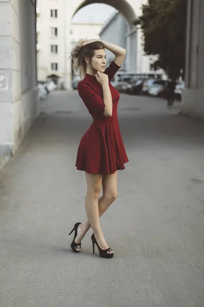 Nice tanned stylish brunette girl in red short dress with flowers is standing poses and flirting walking on the street city