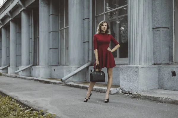 Schön gebräunt stilvolle Brünette Mädchen in rotem kurzen Kleid mit Blumen steht Posen und flirtet zu Fuß auf der Straße Stadt Stockbild