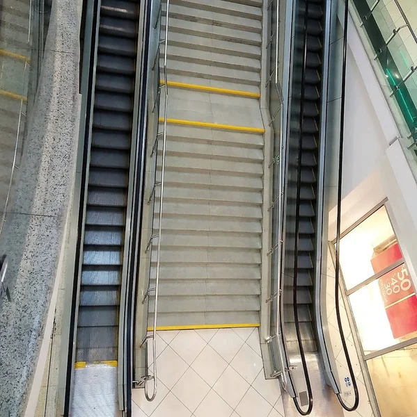 ladder from granite with the nickelized hand-rail, the escalator at the left and on the right with rubber hand-rail, shopping center, a gray ceramic tile, glazing, business