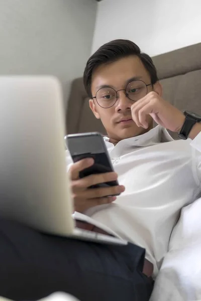 Jóvenes musulmanes malayos trabajando con el ordenador portátil en la cama mirando el teléfono — Foto de Stock