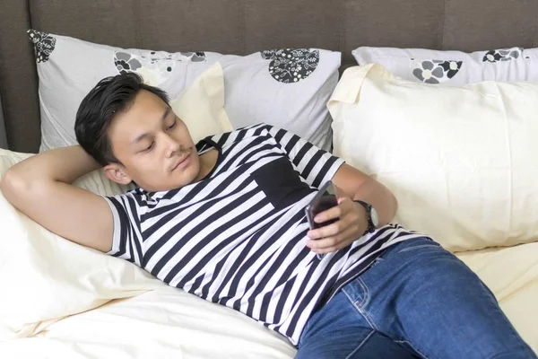 Joven malayo mirando el teléfono relajándose en la cama — Foto de Stock
