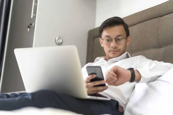 Jóvenes musulmanes malayos trabajando con el portátil en la cama mirando a la hora — Foto de Stock