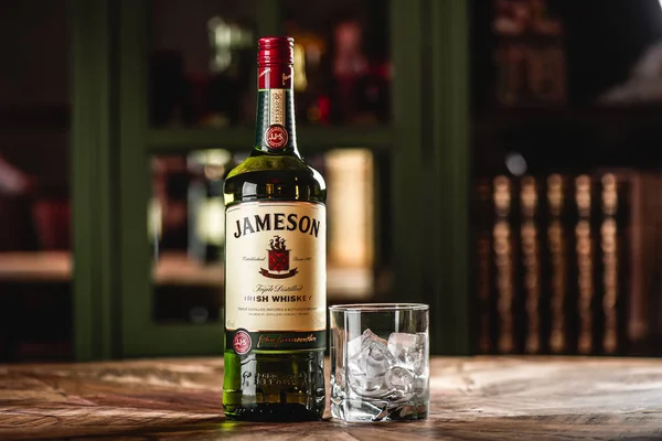 詹姆森威士忌瓶和玻璃在木桌上的冰块在黑暗的酒吧 詹姆森是来自都柏林的传统爱尔兰威士忌品牌 — 图库照片