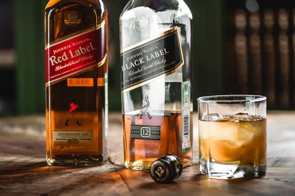 赤ラベルと黒ラベルのウイスキーのボトルと木製のテーブルにアイス キューブ ガラス ジョニー ウォーカーはスコッチ ウイスキーをブレンドし 世界で有名なブランドの一つ — ストック写真