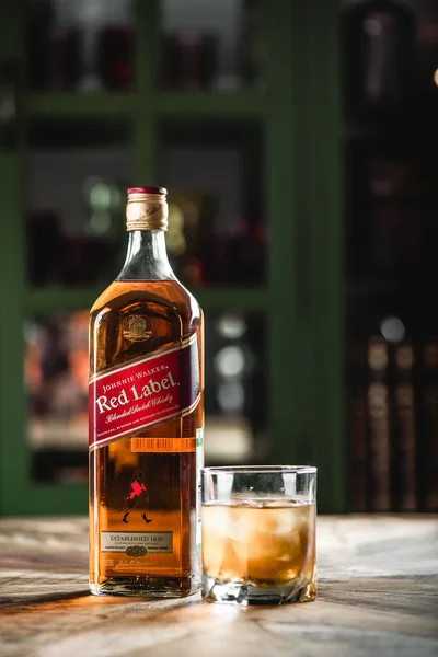 Kırmızı etiket viski şişe ve cam ahşap masa buz küpleri ile. Johnnie Walker harmanlanmıştır Scotch viski dünyada ünlü markalardan biri ise