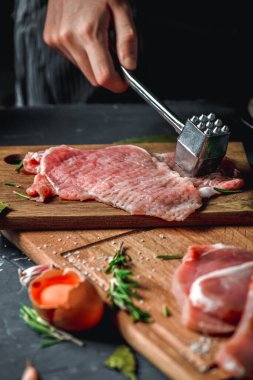 Pirzola ve domuz pirzolası un, biberiye, defne yaprağı ve mutfak masasındaki sosla kesim tahtalarının üzerinde. Şefin elinden bir parça et unun içine düştü. Metin için yer