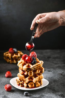 Kahvaltıda Belçika waffle 'ı. Kadın eli tatlı olarak kaşıktan reçel döker. Güzel meyveli waffer keki.