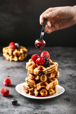 Kahvaltıda Belçika waffle 'ı. Kadın eli tatlı olarak kaşıktan reçel döker. Güzel meyveli waffer keki.