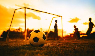 Alacakaranlık günbatımı gökyüzü altında toplum kırsal alanda egzersiz için futbol futbol oynarken eğlenen bir grup çocuk siluet eylem spor açık havada.