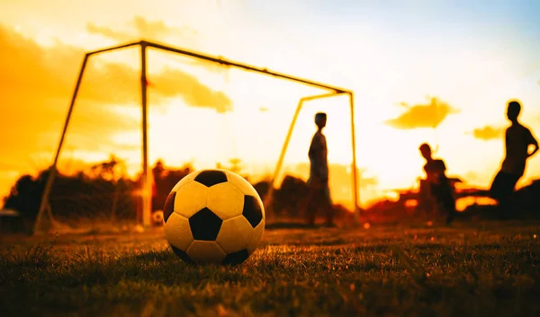 Alacakaranlık günbatımı gökyüzü altında toplum kırsal alanda egzersiz için futbol futbol oynarken eğlenen bir grup çocuk siluet eylem spor açık havada.