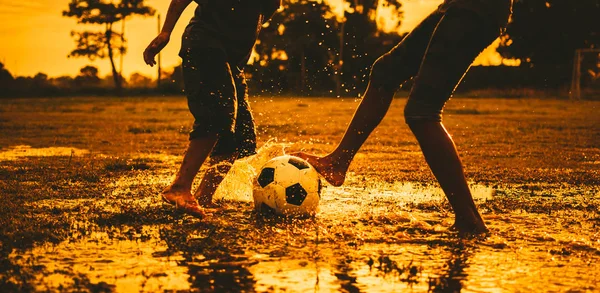 Alacakaranlık günbatımı gökyüzü altında toplum kırsal alanda egzersiz için futbol futbol oynarken eğlenen bir grup çocuk siluet eylem spor açık havada.
