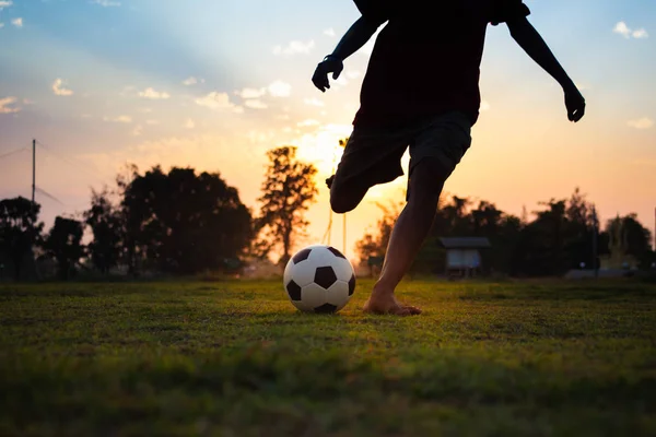 Alacakaranlık günbatımı gökyüzü altında toplum kırsal alanda egzersiz için futbol futbol oynarken eğlenen bir grup çocuk siluet eylem spor açık havada.