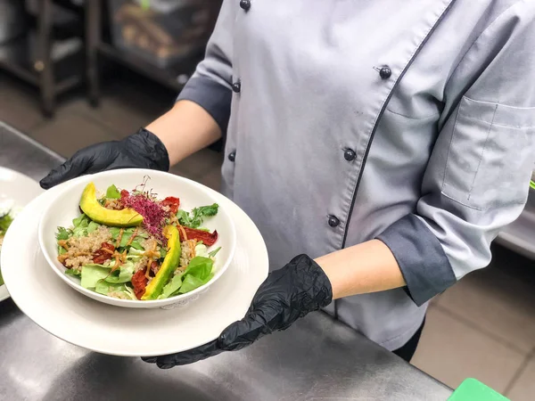 Şef bir plaka restoran mutfağında avokado salatası ile siyah eldiven