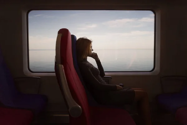 Kız, deniz manzaralı pencerenin yanındaki trende oturuyor.