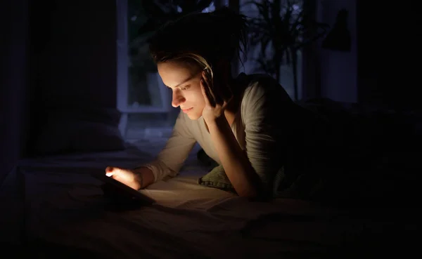 Genç bir kız yatakta yatar ve akıllı telefonuna bakar.