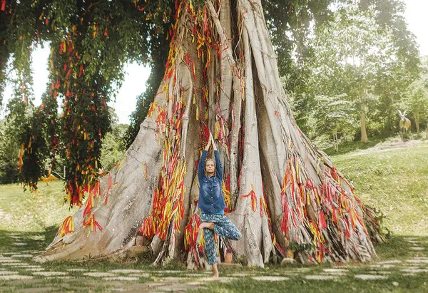 Arka planda ağaçla yoga yapan bir kız.