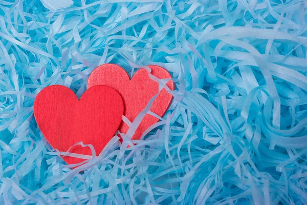 Two red wooden heart lies in blue shredded paper. Romantic background