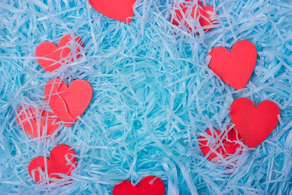 Somewhat red wooden heart lies in blue shredded paper. Romantic background