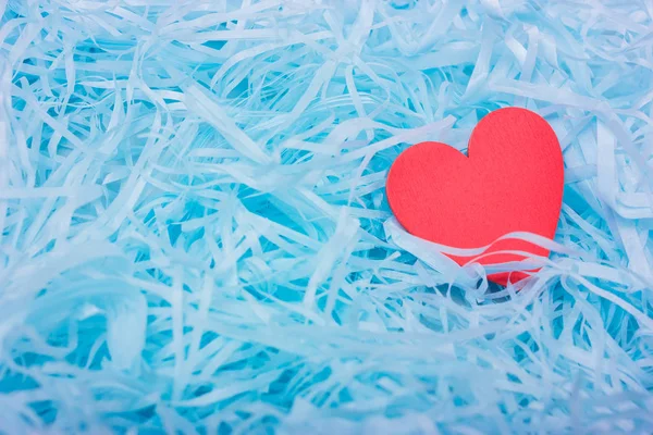 One red wooden heart lies in blue shredded paper. Romantic background