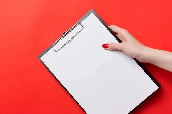 Womans hands with red nails holding black clipboard on red background