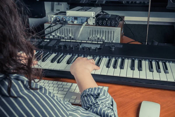 Female musician playing midi keyboard synthesizer in recording studio, focus on hands. Womans arms plays solo of music or new melody. Close-up