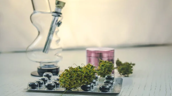 Marijuana knoppar, bong, Grinder och piller ligger på vita bordet. — Stockfoto