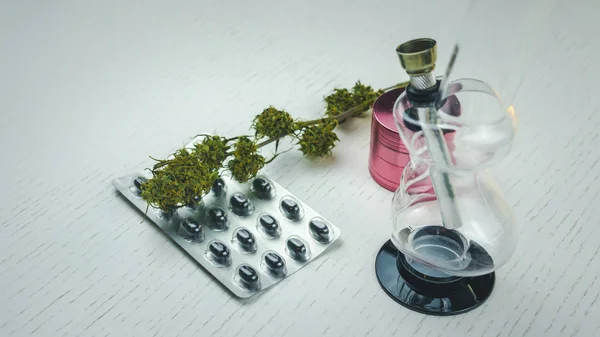 Μπουμπούκια μαριχουάνας, Μπονγκ, μύλος και χάπια βρίσκονται στο λευκό τραπέζι. — Φωτογραφία Αρχείου