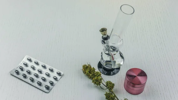 Bourgeons de marijuana, bong, broyeur et pilules reposent sur la table blanche . — Photo