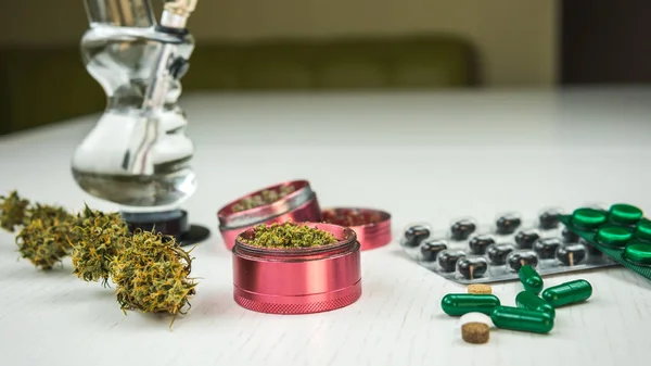 Brotes de marihuana, pipa, molinillo y pastillas yacen sobre la mesa blanca . —  Fotos de Stock