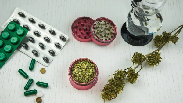 Marijuana buds, bong, grinder and pills lie on the white table. — Stock Photo, Image