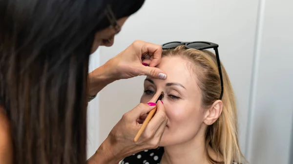 Artista de maquillaje haciendo maquillaje profesional para mujer joven. Mujer a — Foto de Stock