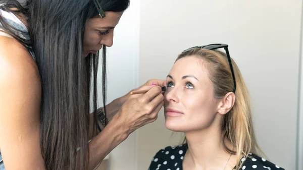 Artista de maquillaje haciendo maquillaje profesional para mujer joven. Mujer a — Foto de Stock