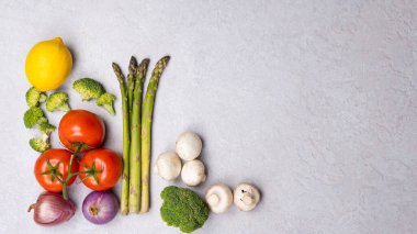 Organik taze sebzeler grubu - yeşil kuşkonmaz, brokoli, gri arka planda mantarlar, düz yatak. Sağlıklı vejetaryen yemek, diyet ve ev yemeği kavramı. Üst görünüm, alanı kopyala.