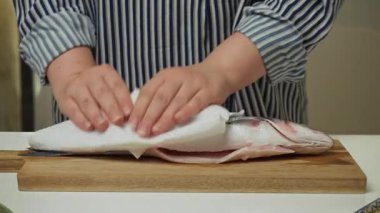 Kadın elleri, levrek balığını ev mutfağında pişirmek için hazırlıyor. Sağlıklı beslenme ve deniz ürünleri kavramları
