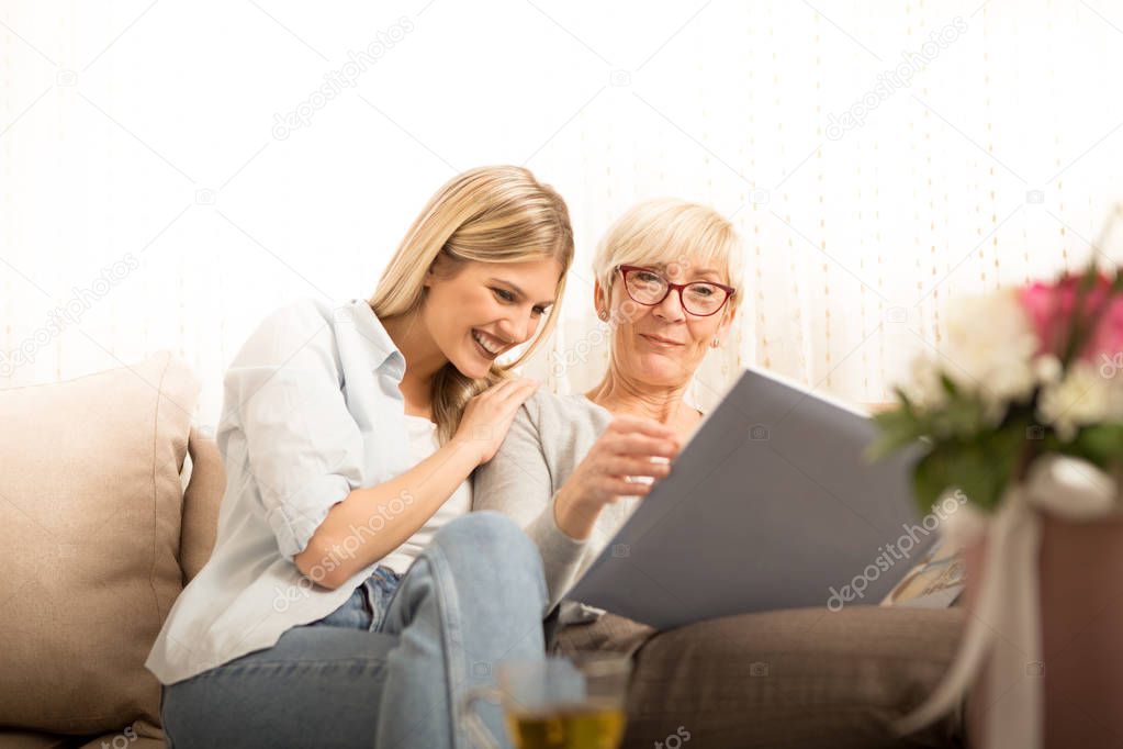Mother and daughter watch a family photo album, remembering beautiful moments.