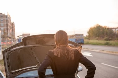 Güzel esmer, bozuk arabasının kaputunun altına bakar ve ne yapacağını bilmez..