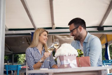 Güzel sarışın kız ve yakışıklı genç adam beyaz şarap içip yıldönümlerini kutluyorlar..