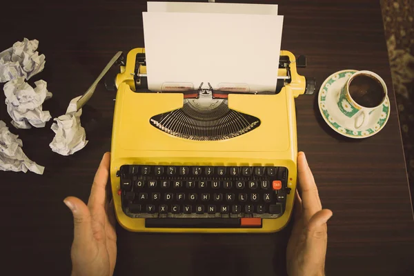 The writer sits in front of an old yellow typewriter, waiting for writing inspiration to appear.