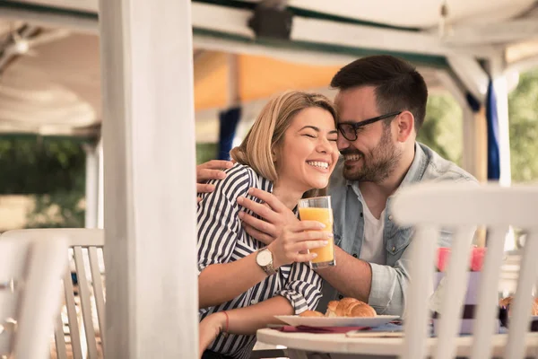 Restoranın bahçesinde kahvaltı yaparken kız arkadaşına sarılan yakışıklı bir genç..