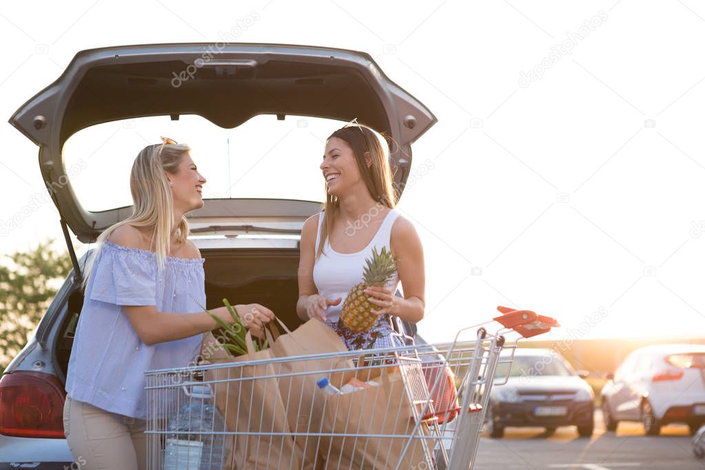 two beautiful girls puts groceries in his car in front of a supermarket.
