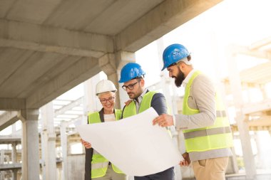 Tatmin olmuş takım bina planlarına bakıyor. Takım bir kadın ve iki erkekten oluşuyor. Tatmin olmuş görünüyorlar..
