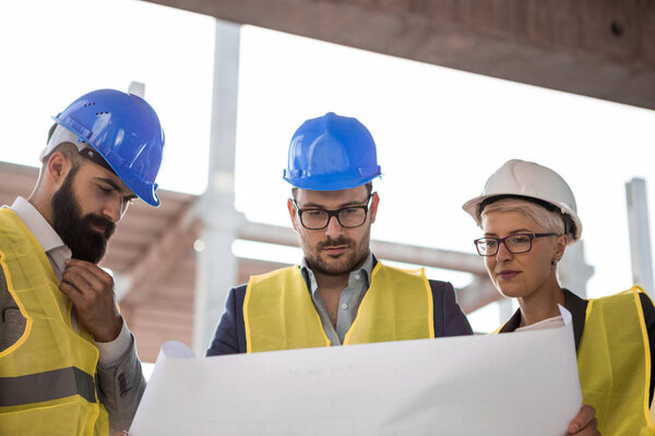 Architects look at the blueprints and inspect the situation on the construction site.